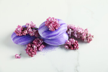 Soap bars, sea salt and lilac flowers on white marble table, closeup