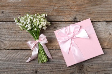 Bouquet of beautiful lily-of-the-valley flowers and gift on wooden background, top view