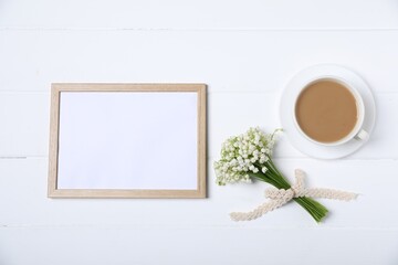 Bouquet of beautiful lily-of-the-valley flowers, coffee and blank frame on white wooden background, flat lay