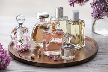 Bottles of perfumes and lilac flowers on white wooden table, closeup
