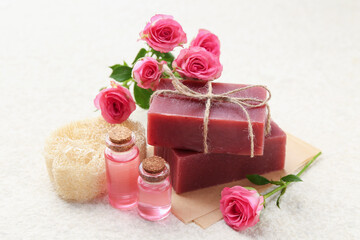 Soap bars, loofah sponge, essential oils and beautiful roses on beige table, closeup