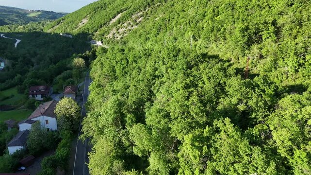 Aerial view of Mignano Dam, capturing its sweeping concrete arc, tranquil reservoir, and the lush, rolling hillsides of the Arda valley, dotted with houses and winding rural roads, PC, Italy