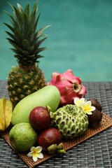 Different tropical fruit on wicker table near swimming pool