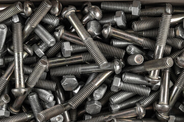 A close-up shot of a pile of various metallic bolts and screws, showcasing their textures and details. The image emphasizes the industrial nature of the hardware