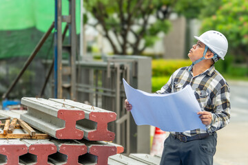 Construction engineer wea safety helmet and glasses examining blueprints at building site du...