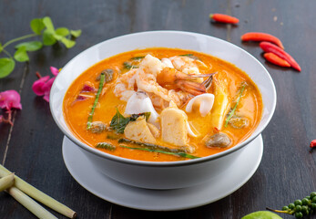 A bowl of Tom Yum soup with shrimp, squid, and mushrooms.