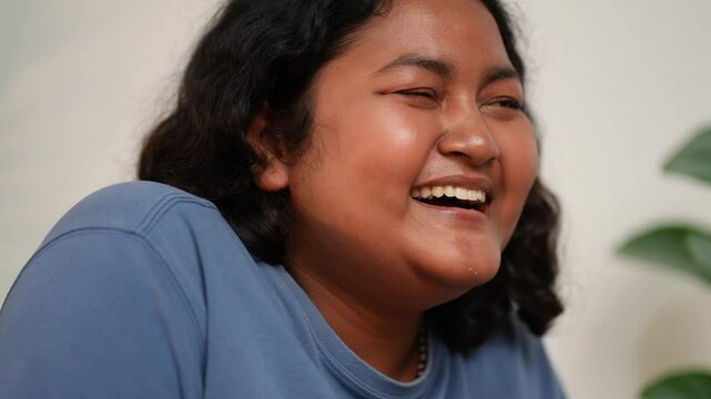 Joyful Asian woman laughing with a radiant smile in a candid moment, capturing genuine happiness, natural beauty, and warmth in a serene atmosphere filled with peaceful and positive energy