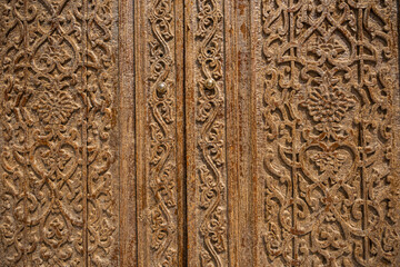 Traditional Islamic wooden door with intricate carved floral and geometric patterns close up,...