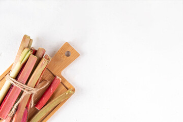 Raw fresh organic rhubarb stems on kitchen table background, bunch of homegrown pink and green rhubarb ready for cooking, on cutting board. Summer harvest, summer food and dessert cooking ingredient