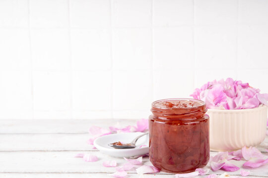 Rose petals jam, sweet tasty flower dessert, homemade confiture preserves with organic dessert roses petals, sugar and honey, in small jar on white table. Alternative medicine, remedies for sore throa