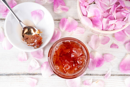 Rose petals jam, sweet tasty flower dessert, homemade confiture preserves with organic dessert roses petals, sugar and honey, in small jar on white table. Alternative medicine, remedies for sore throa