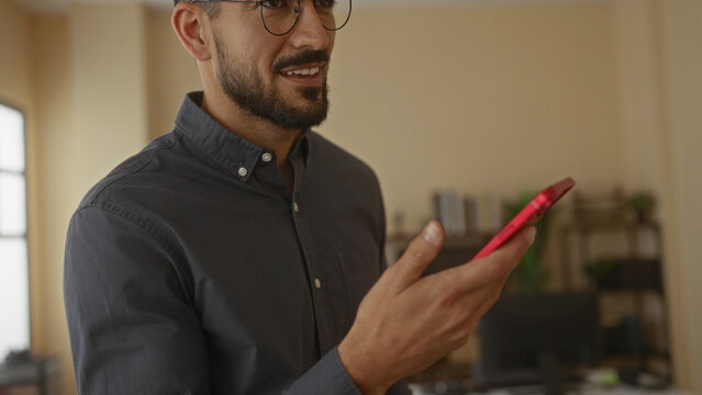 Young man talking on smartphone in modern office wearing glasses and casual shirt showcasing professional atmosphere and confident demeanor in workplace interior setting.