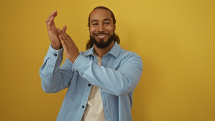 Man with beard clapping over yellow background wearing light blue shirt exhibiting joy and positive...