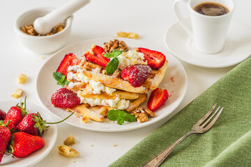 Belgian waffles with whipped cream, strawberries and walnuts on a white plate with a cup of aromatic coffee. Summer dessert for breakfast.