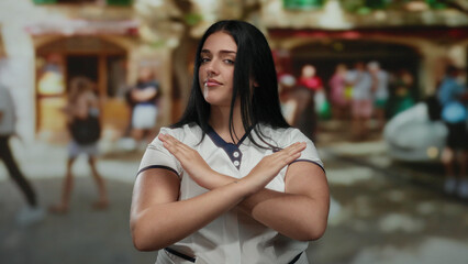 Young plus-size woman standing on a busy city street making an x gesture with her arms, expressing disapproval in an outdoor urban environment.