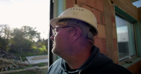 Side profile of mature construction worker in hard hat looking outdoors, standing near doorway,...