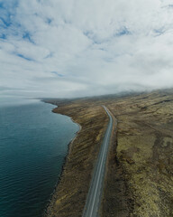 Fototapeta premium Aerial view of coastal road winding through misty Faskrudsfjordur, Iceland...