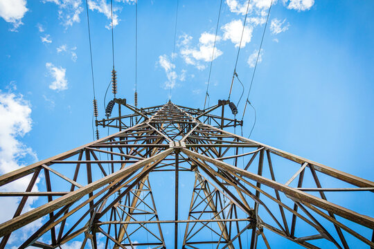 Electricity transmission tower photographed from below with high-voltage lines against a clear blue sky, suitable for energy, technology, or industrial themes