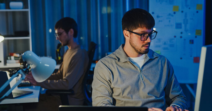 Team adult male freelance developer work late typing write prompt AI bot app program nomad terminal code at office night. Artificial intelligence dashboard, robotics, user interface, machine learning.