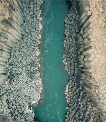 Aerial view of turquoise river slicing through basalt columns, Studlagil Canyon...