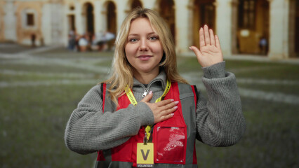 Woman volunteer performing oath gesture in an outdoor university setting, wearing a red vest and...