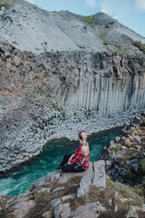 Woman sits on cliff edge overlooking basalt columns in Studlagil Canyon...