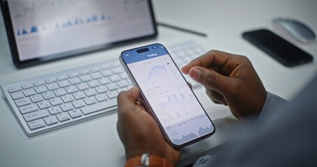 Financial Analyst Checking Real-Time Stocks, Exchange Market Charts on Smartphone and Digital Tablet Using Online Trading App. African American Businessman Working in Investment Bank Office. Close Up.