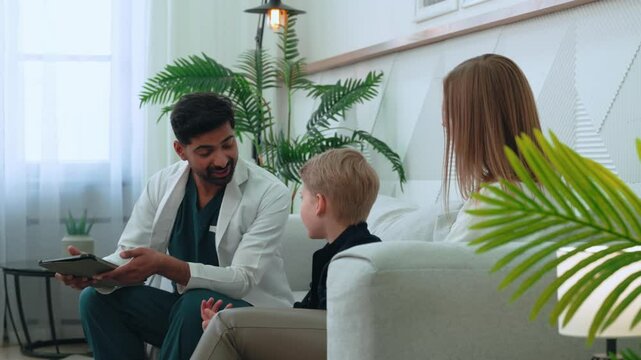 Medical professional reviewing patient health details on digital tablet while consulting with child and mum parent, displaying empathetic medical care in bright hospital environment