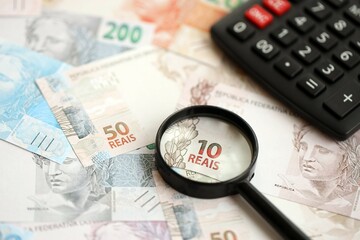 Brazilian reais banknotes and calculator with magnifying glass. Brazil real money, calc with loupe