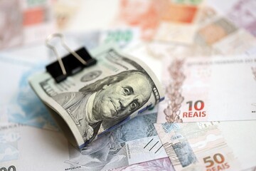 Bunch of US dollar bills lies on big amount of Brazilian reais banknotes close up