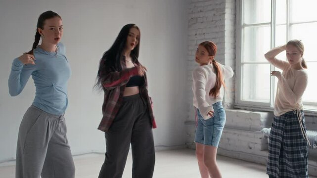 Zoom in slowmo shot of four gen Z Caucasian girls in urbanwear moving freely and then looking at camera in minimalist dance studio, copy space