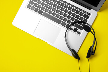 Headset with microphone and laptop on yellow background, top view