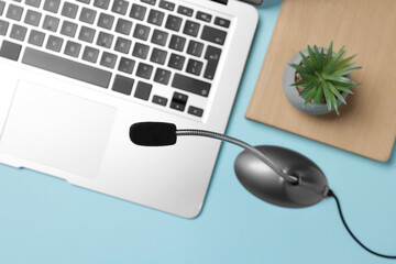 Professional microphone, laptop, notebook and floral decor on light blue background, flat lay