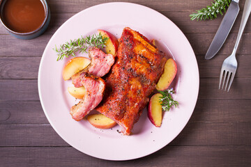 Roasted rack of pork ribs with apples on a plate and brown wood background. High angle view