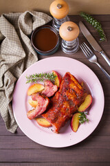 Roasted rack of pork ribs with apples on a plate and brown wood background. High angle view