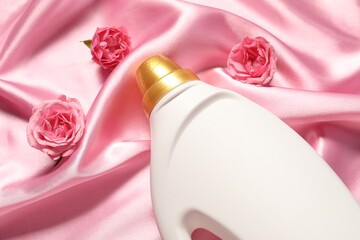 Bottle of fabric softener and flowers on pink cloth, above view