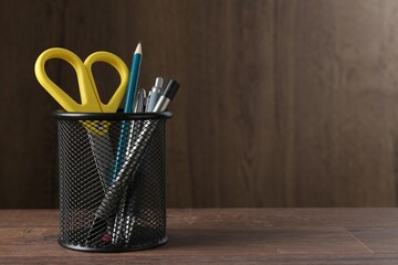 Pens and other stationery in holder on wooden table, space for text