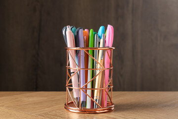 Many different pens in holder on wooden table