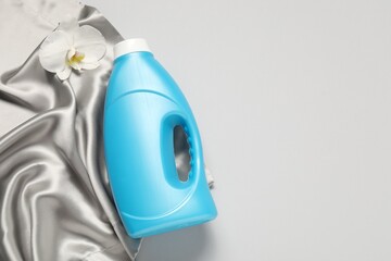 Bottle of fabric softener, orchid flower and color cloth on light grey background, flat lay. Space for text