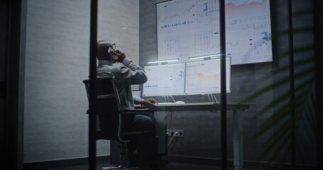 Financial Analyst Suffering from Financial Crisis, Yelling in Phone, Analyzing Exchange Market Charts in Office at Night. African American Businessman Furious About Sudden Stock Market Collapse.