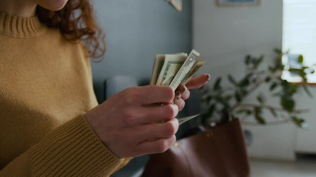 Close-up shot of unrecognizable woman in yellow sweater counting stack of five-dollar bills in bank office