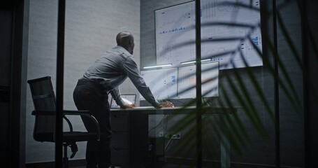 Financial Analyst Suffering from Financial Crisis, Yelling in Phone, Analyzing Real-Time Market Charts in Office at Night. African American Businessman Furious About Sudden Stock Market Collapse.