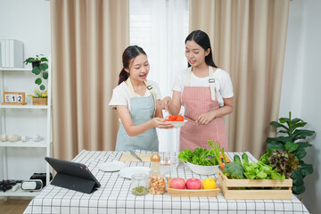 Asian young two women cooking salad in kitchen. Active beautiful girl feel happy and enjoy eating vegetables healthy foods to diet and lose weight for health care in house
