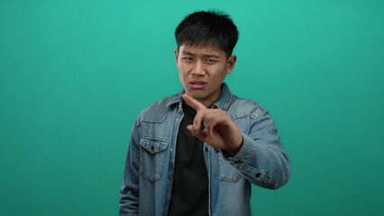 Young man gesturing no with his finger against an isolated green background conveying disapproval