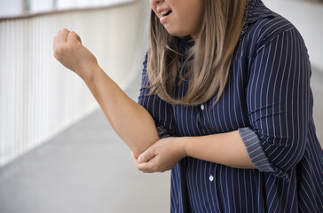 Plus-sized chubby Asian middle-aged aunt woman suffering from tennis elbow syndrome or elbow joint pain or injury, injured elbow tendon, rheumatoid or gout arthritis concept