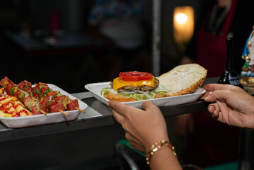 Close-up of a freshly prepared burger, garnished with various toppings, resting on a disposable white tray