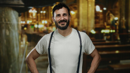 Obraz premium Hispanic man with beard in white shirt smiling confidently inside a traditional catholic church with ornate architecture and warm lighting.