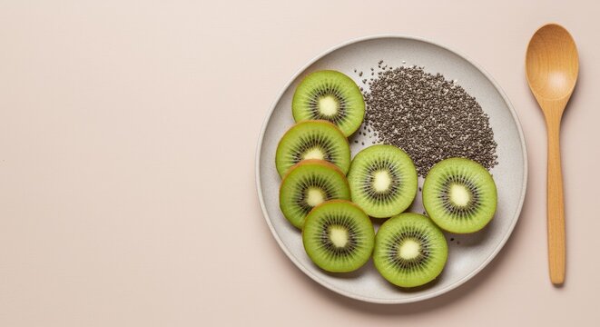 Top view of fresh kiwi slices and chia seeds on ceramic plate with wooden spoon on pastel background