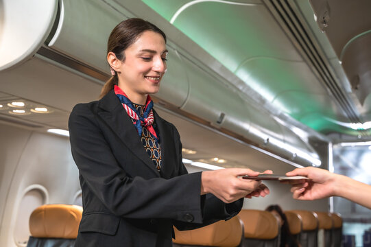 Friendly Caucasian female flight attendant in airline uniform checking passport on board, airline business concept