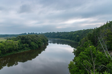 Peaceful landscape of the Grand River winding through lush green forest under a cloudy sky near Kitchener and Cambridge, Ontario, Canada.